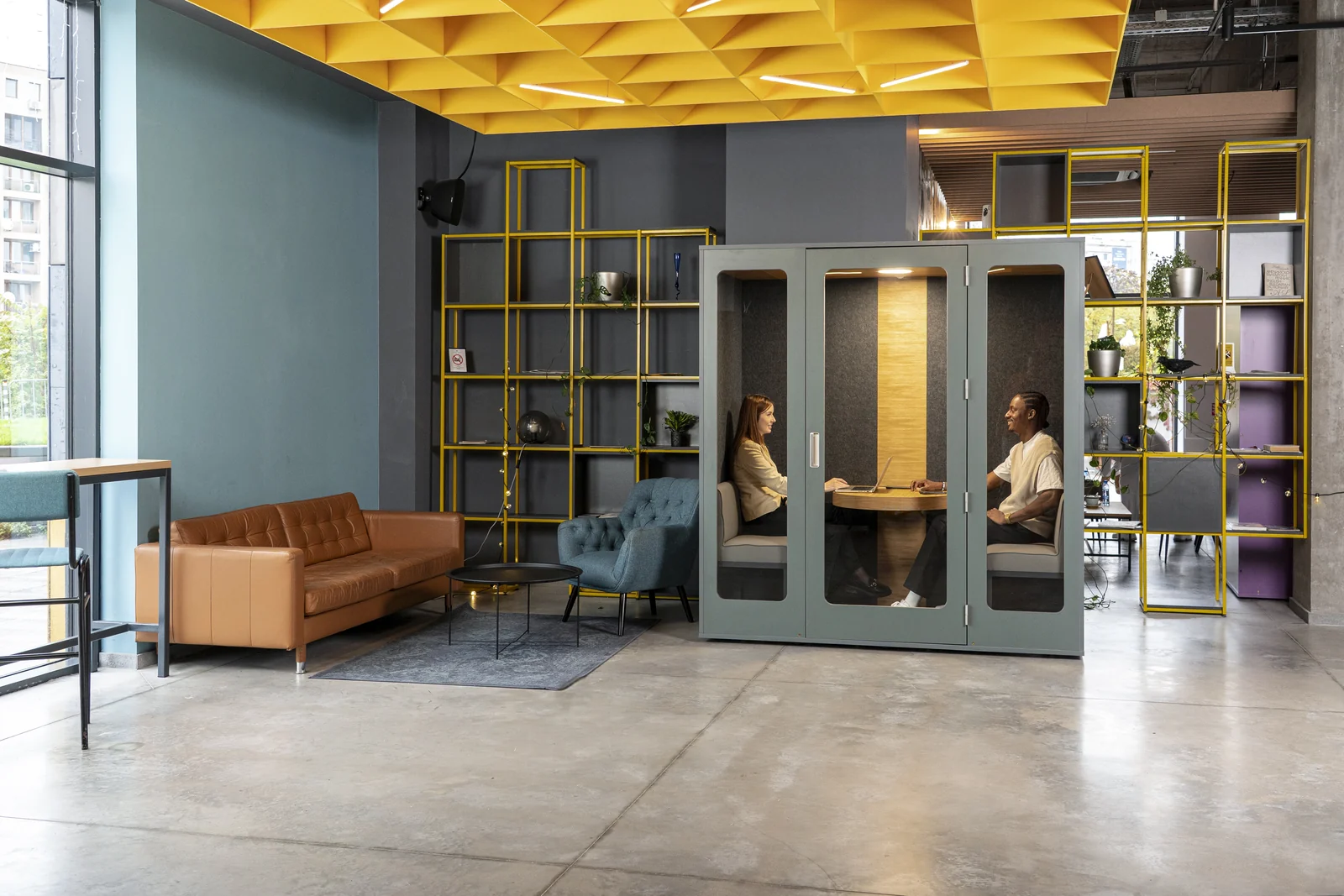 Two people meeting in a grey-green MEAVO Camden pod beside yellow shelving